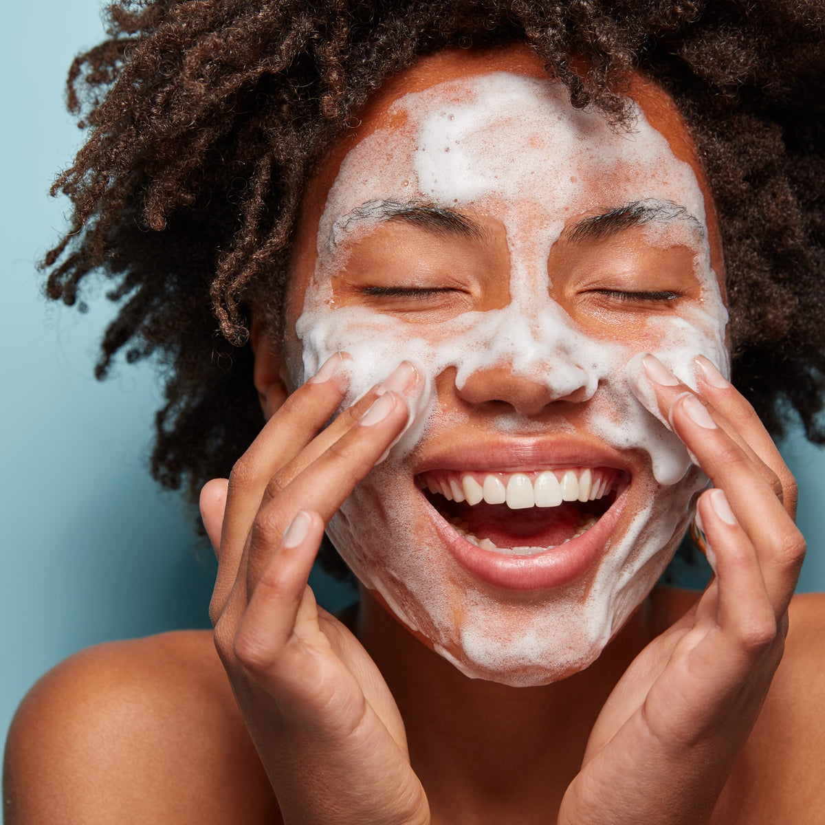 femme souriante se nettoyant le visage avec de la mousse